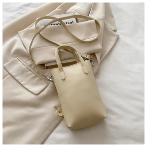 Mini borsa a tracolla crema con doppi manici ad anello su sfondo di un blazer