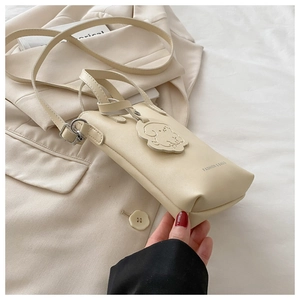 Close-up of cream crossbody phone bag with dog charm and fashion text detail