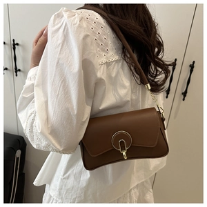 Detail of a brown leather shoulder bag with a gold metal ring buckle and white lace shirt
