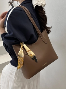 Dark brown leather tote bag with white stitching and floral scarf on a model