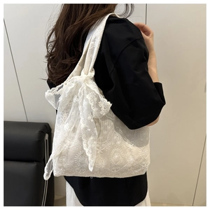 Detailed view of white lace tote bag with floral embroidery and large side bow decoration