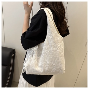 Detail of white lace floral embroidery on a shoulder bag worn by a model in a side view