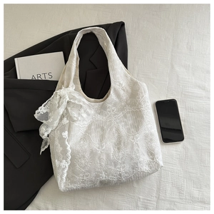 Detailed macro view of white floral lace tote bag with large decorative bow on white surface