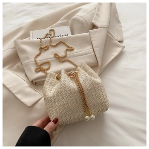 Detail of straw woven bucket bag featuring gold chain strap and elegant pearl drawstring