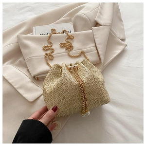 Close-up of beige straw bucket bag with gold chain strap and elegant pearl drawstring