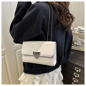 Detail of white crocodile pattern shoulder bag with silver chain strap on a model