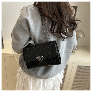 Detail of black crocodile texture crossbody bag with silver chain strap on model