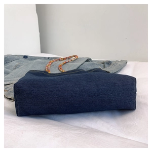 Dettaglio della base di una borsa a tracolla in denim retrò con tracolla perlata