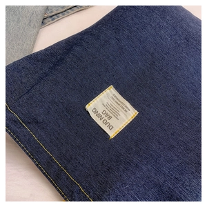 Dettaglio macro della trama denim con etichetta tessuta bianca e cuciture gialle a contrasto