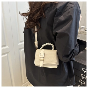 Detail of beige crossbody bag featuring pearl handle and straw woven flap with gold buckle