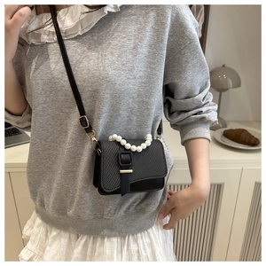 Detail of black crossbody bag with large pearl handle and woven texture on front flap