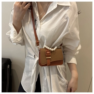 Detail of tan leather crossbody bag with woven flap and decorative pearl handle