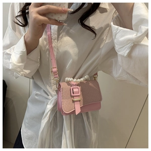 Pink crossbody bag with pearl handle and woven texture flap detail on white shirt