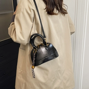 Retro black glossy shell bag with gold hardware and woven charm worn with a trench coat