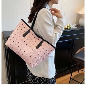 Detail of pink tote bag with black bow patterns and pleated texture on shoulder