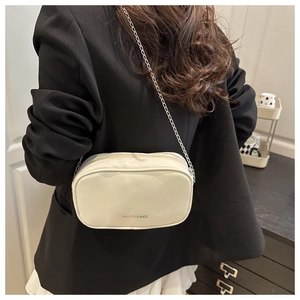 Petit sac bandoulière crème avec chaîne porté sur une veste de blazer noire chic