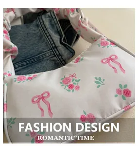 Detail of white canvas underarm bag with pink rose and bow prints on denim backdrop