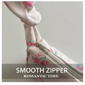Detail of smooth metal zipper and pink rose floral print on a white fabric handbag