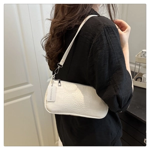 Detail view of a white crocodile embossed baguette bag worn by a model on shoulder