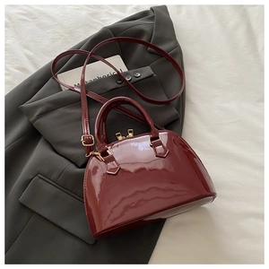 Dettaglio borsa a conchiglia bordeaux in vernice su blazer grigio e hardware oro