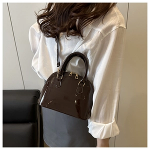 Detail view of glossy dark brown shell bag with gold hardware and smooth zipper