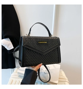 Detail of black woven texture handbag with V-shaped flap and top handle for commuting