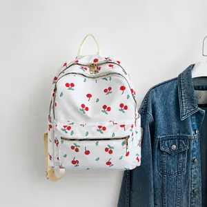 Detail showing white nylon backpack with red cherry pattern hanging on a wooden hook