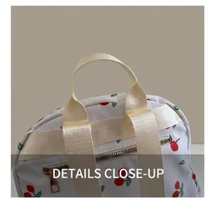 Close-up of durable cream nylon handle and golden metal zippers on cherry print backpack