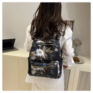Detailed view of water-resistant floral nylon backpack with golden metal zippers on a model