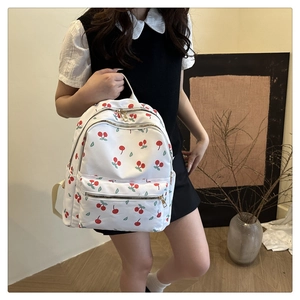 Detailed view of white cherry print backpack with metallic zippers and nylon texture