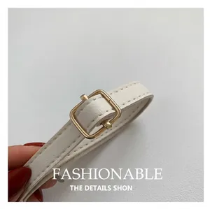 Detail of white leather shoulder strap with gold buckle and neat stitching on straw bag