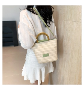 Detail of woven straw bucket bag with green leather trim and wooden handle