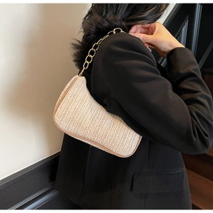 Detail of straw woven baguette bag with gold chain strap on a black blazer