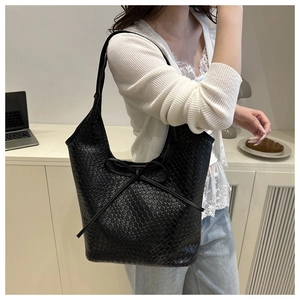 Detail view of black woven tote bag with bow decoration worn by model in home setting