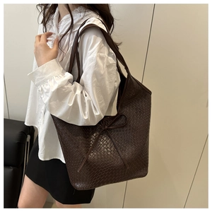 Detail of dark brown woven tote bag featuring a bow accent and premium leather texture