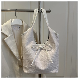 Detailed view of cream-white woven leather tote bag with a minimalist bow decoration