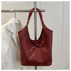 Detail of burgundy woven leather tote bag with elegant bow accent and textured finish