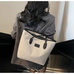 Close-up of a minimalist cream canvas tote bag with black leather trim on a model