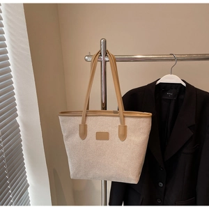 Detailed view of beige canvas tote bag with brown leather trim hanging on a metal rack