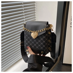 Détail du sac bandoulière noir avec chaîne de cœur dorée et large sangle textile