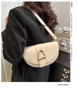Chic beige saddle bag with gold D-buckle detail shown worn by a model in soft lighting