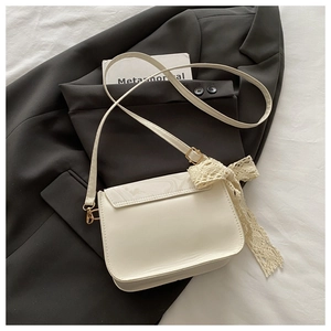 Detail of cream white leather crossbody bag featuring lace bow and gold-tone hardware