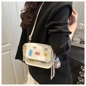 Detailed shot of a white crossbody bag with colorful patches and a plush doll charm