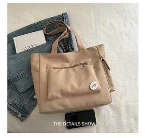Detail view of large beige canvas tote bag showing front zip pocket and side storage pouch
