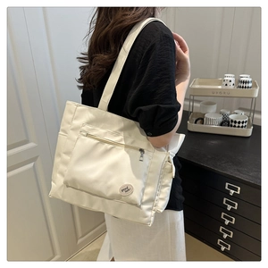 Detail of cream nylon tote bag featuring front zipper pocket and good luck embroidery