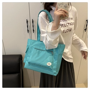 Blue nylon tote bag showing front zipper pocket and decorative 'good luck' patch detail