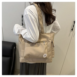 Détail du grand sac cabas en toile beige avec poche zippée et écusson décoratif chic