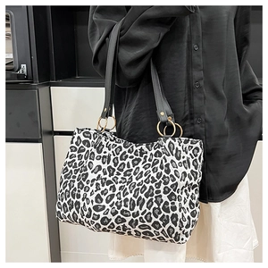 Detail of leopard print tote bag featuring black leather handles and gold metal rings