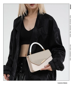 Detail of two-tone cream handbag with horizontal texture and gold bar closure