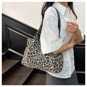 Detail of leopard print canvas tote bag featuring black leather straps and gold metal rings